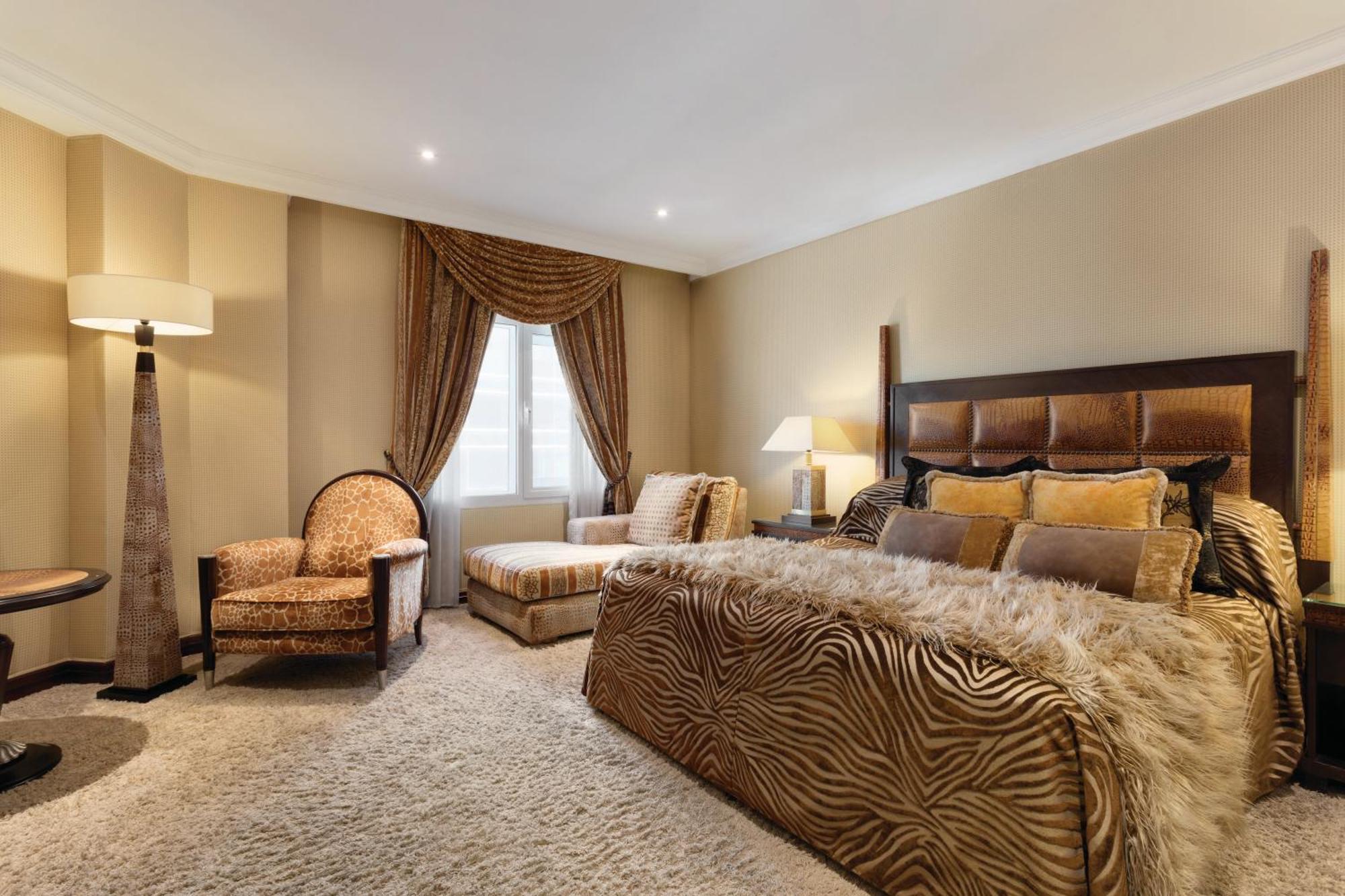 Grand Regency Doha, Trademark Collection By Wyndham Luaran gambar The photo shows a stylishly decorated bedroom. The focal point is a large bed dressed in fabrics with a rich, textured appearance, possibly featuring a zebra print or similar design. On either side of the bed, there are small bedside lamps. 

Adjacen