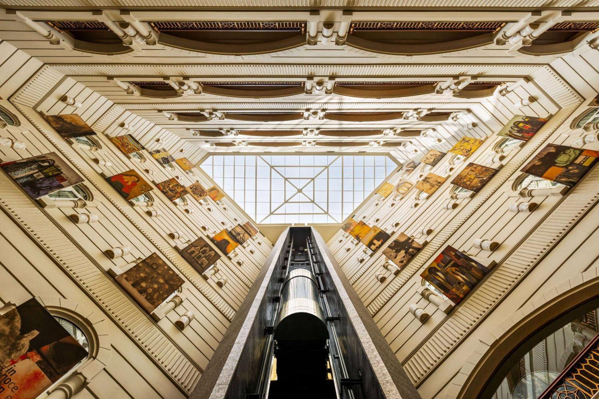 Grand Regency Doha, Trademark Collection By Wyndham Luaran gambar The photo shows an interior view of a building, captured from a low angle looking upwards. The architectural design features a tall, open space with walls adorned with various artworks. In the center, there is a glass ceiling that allows natural ligh