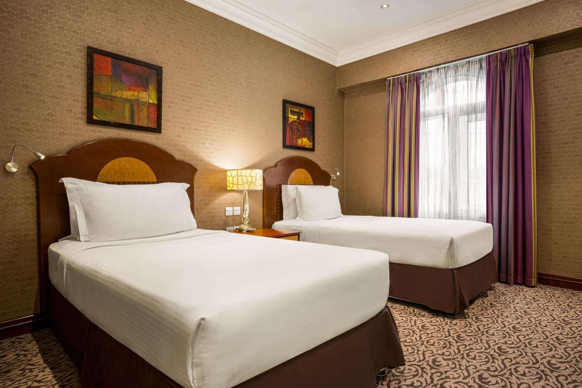 Grand Regency Doha, Trademark Collection By Wyndham Luaran gambar The photo shows a hotel room featuring two single beds with white bedding and dark brown upholstered headboards. There is a bedside table with a lamp between the beds. On the walls are two abstract paintings, and large windows dressed with sheer curt
