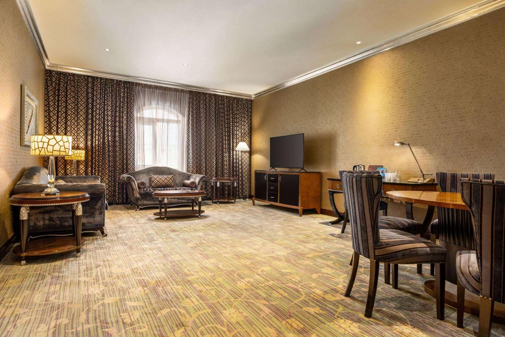 Grand Regency Doha, Trademark Collection By Wyndham Luaran gambar The photo shows a spacious lounge or living area. It features a comfortable seating arrangement with a dark-colored sofa and armchairs, arranged around a coffee table. There's a dining table with matching chairs, suggesting it can accommodate meals o